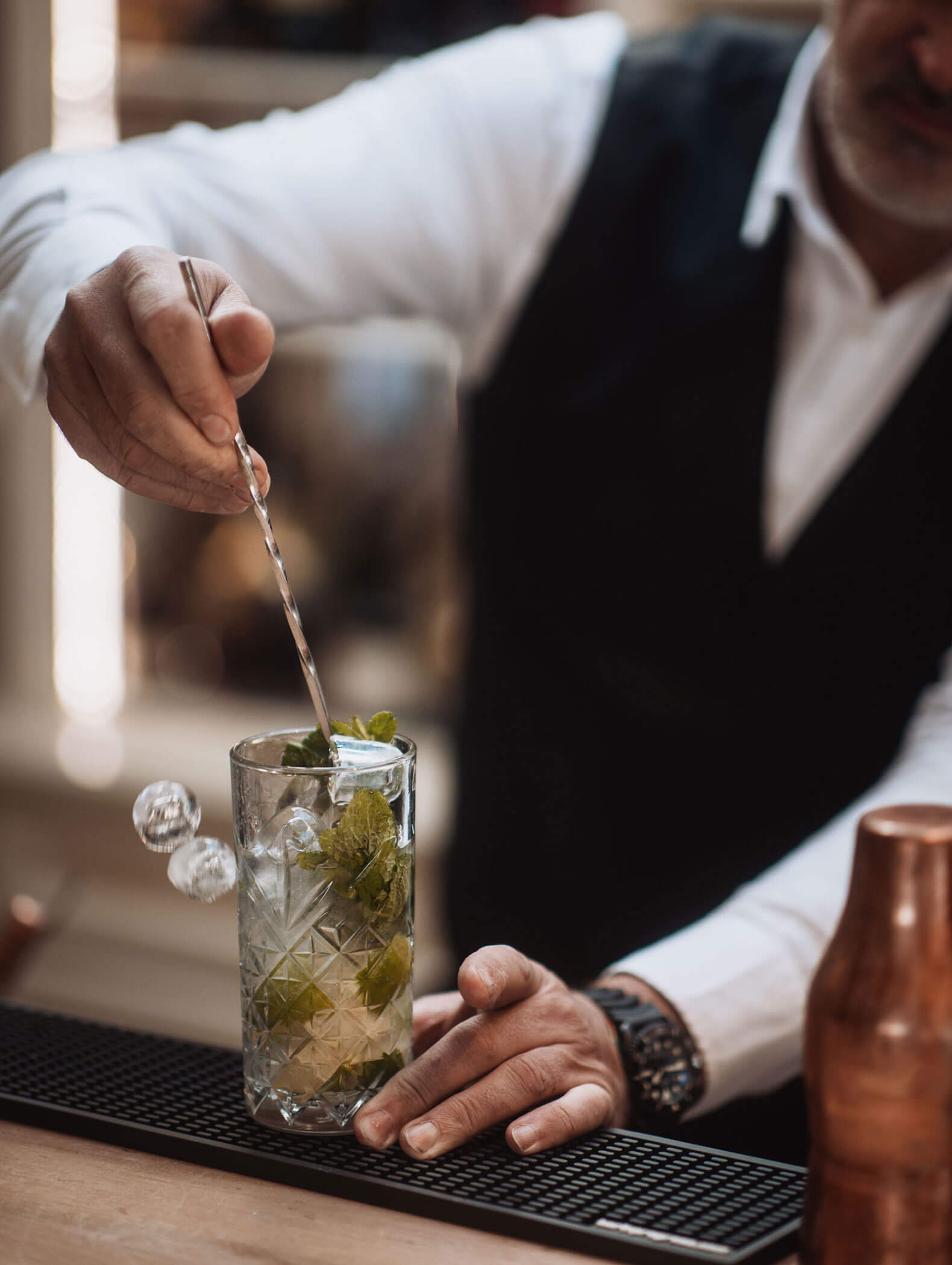 Ein Barkeeper rührt einen Cocktail mit Minzblättern in einem Glas auf einem Bartresen. - Majestic Resorts (Relaunch)