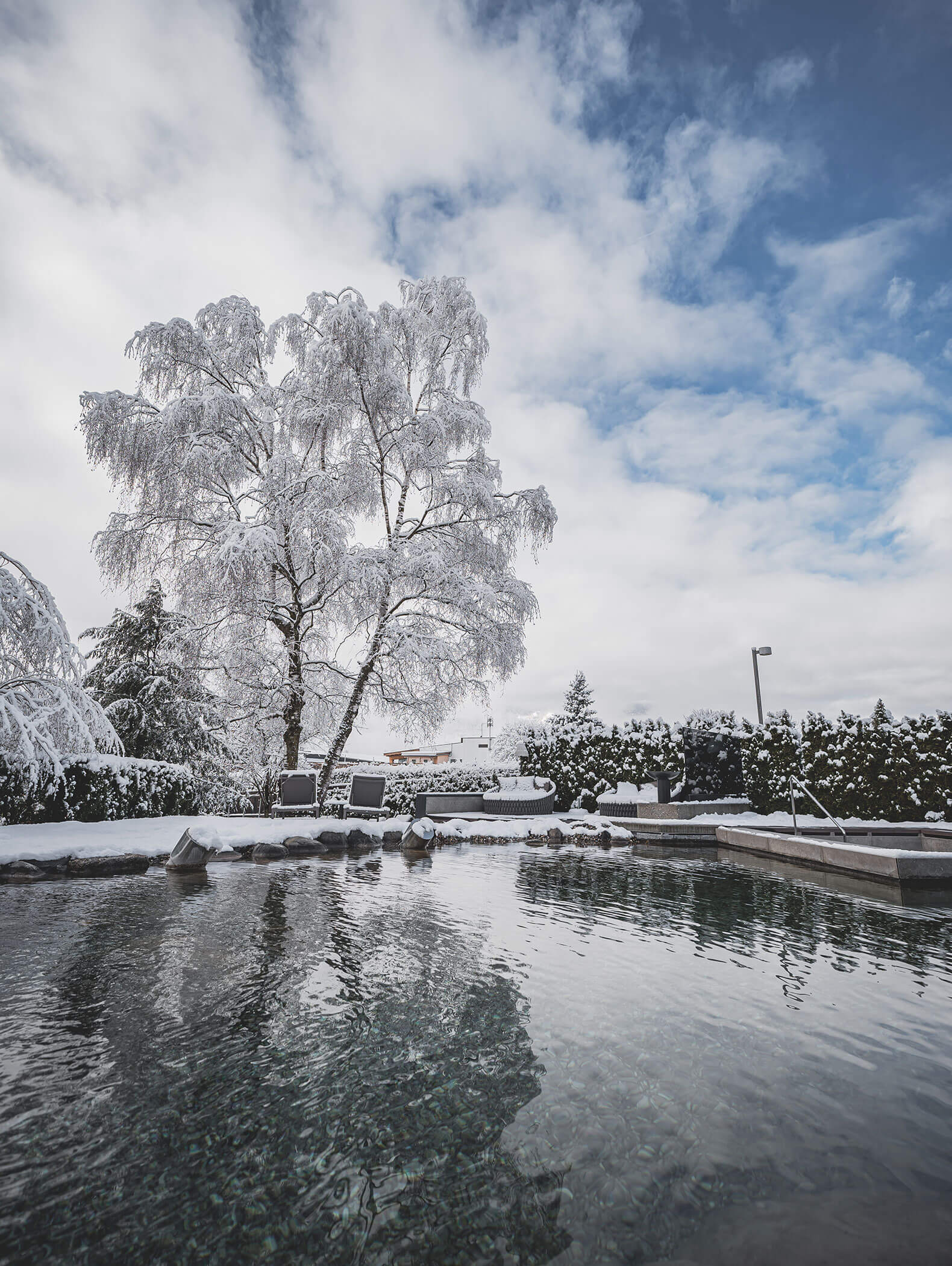 Schneebedeckte Bäume und Sträucher umgeben einen ruhigen Außenpool unter einem teilweise bewölkten blauen Himmel. - Majestic Resorts (Relaunch)