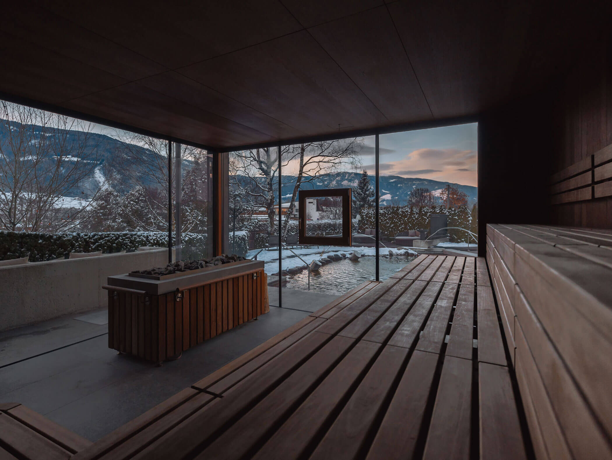 Moderner Saunaraum aus Holz mit großen Fenstern und Blick auf eine verschneite Landschaft und Berge bei Sonnenuntergang. - Majestic Resorts (Relaunch)