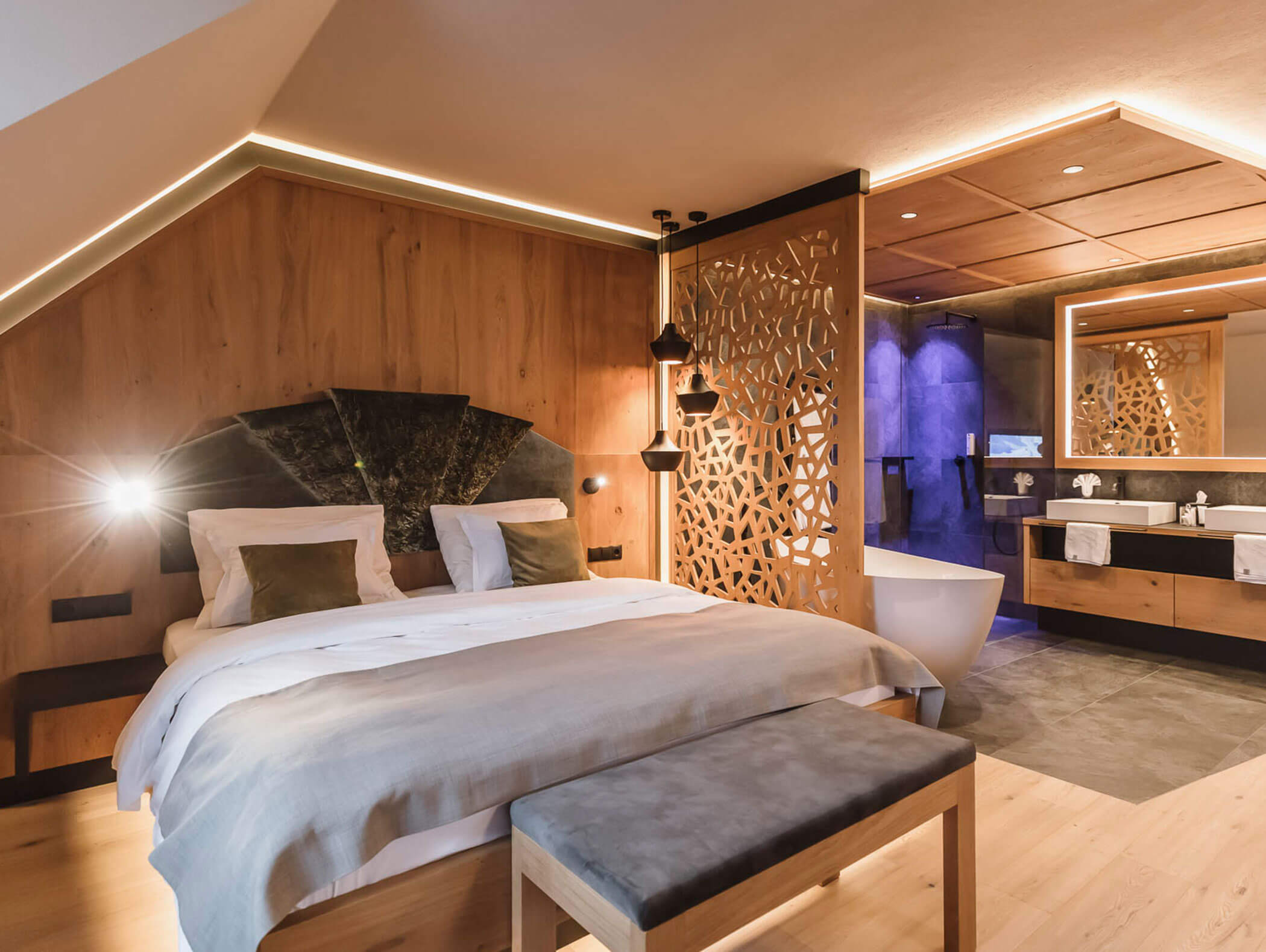 Gemütliches, modernes Schlafzimmer mit Holzakzenten, Doppelbett, freistehender Badewanne und beleuchtetem Badezimmer. - Majestic Resorts (Relaunch)