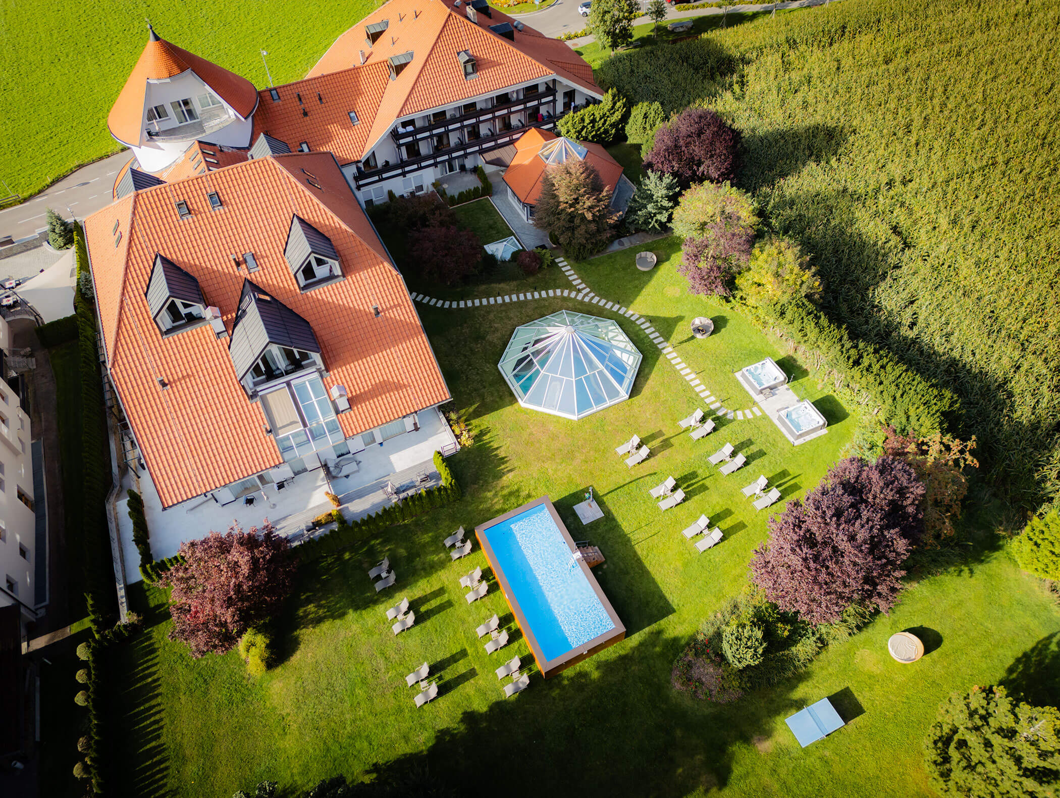 Luftaufnahme eines Hotels mit rotem Dach, Pool, Liegestühlen, Pavillon und grünem, von Bäumen umgebenen Garten. - Majestic Resorts (Relaunch)