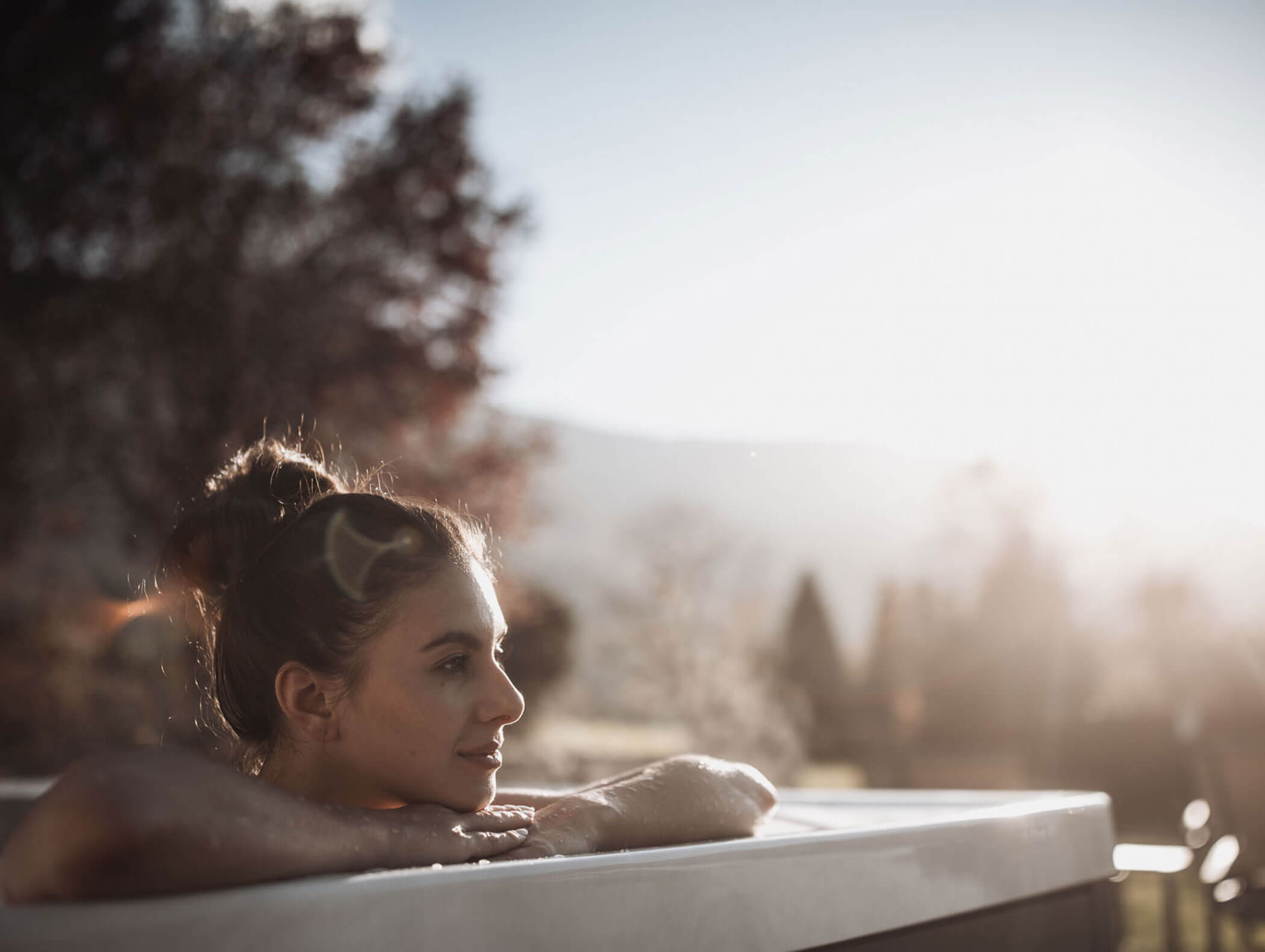 Eine Frau entspannt sich in einem Whirlpool im Freien und blickt nachdenklich auf die sonnenbeschienene Landschaft. - Majestic Resorts (Relaunch)