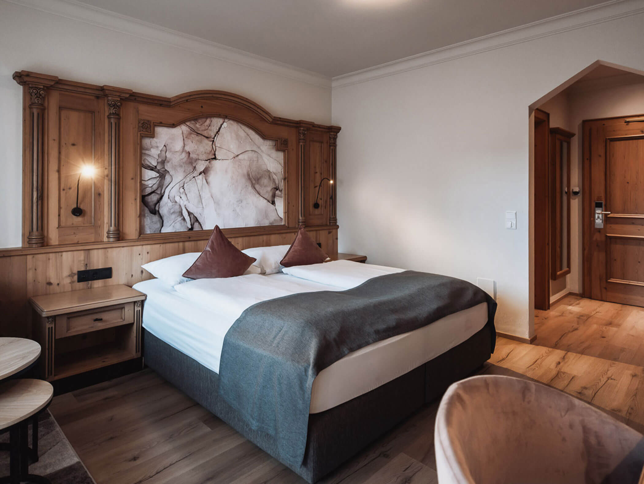 Gemütliches Hotelzimmer mit einem Doppelbett, Kopfteil aus Holz, zwei braunen Kissen und einer grauen Decke. - Majestic Resorts (Relaunch)