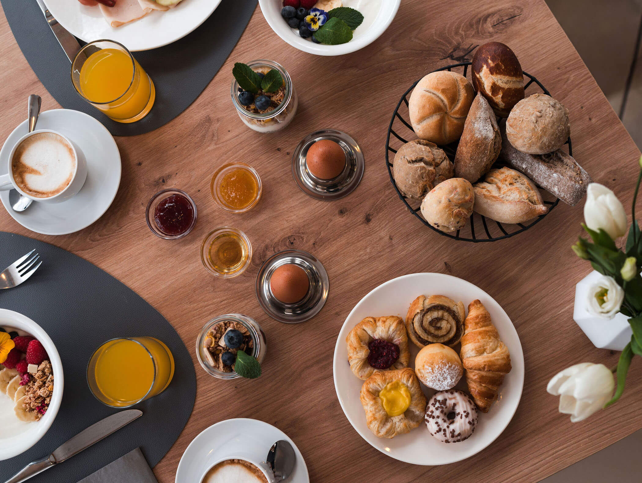Frühstückstisch mit Gebäck, Brötchen, Eiern, Obst, Kaffee, Saft und kleinen Gläsern mit Marmelade. - Majestic Resorts (Relaunch)