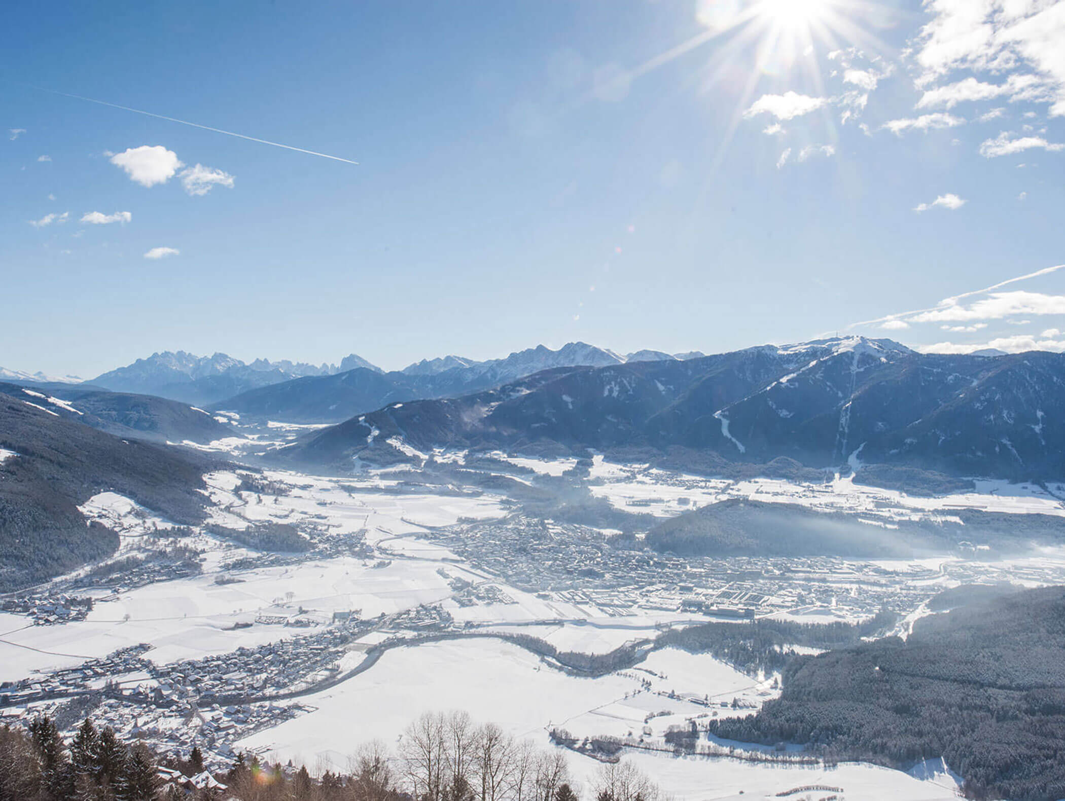 Ein schneebedecktes Tal und eine von Bergen umgebene Stadt unter einem hellen, sonnigen Himmel mit einem sichtbaren Kondensstreifen. - Majestic Resorts (Relaunch)