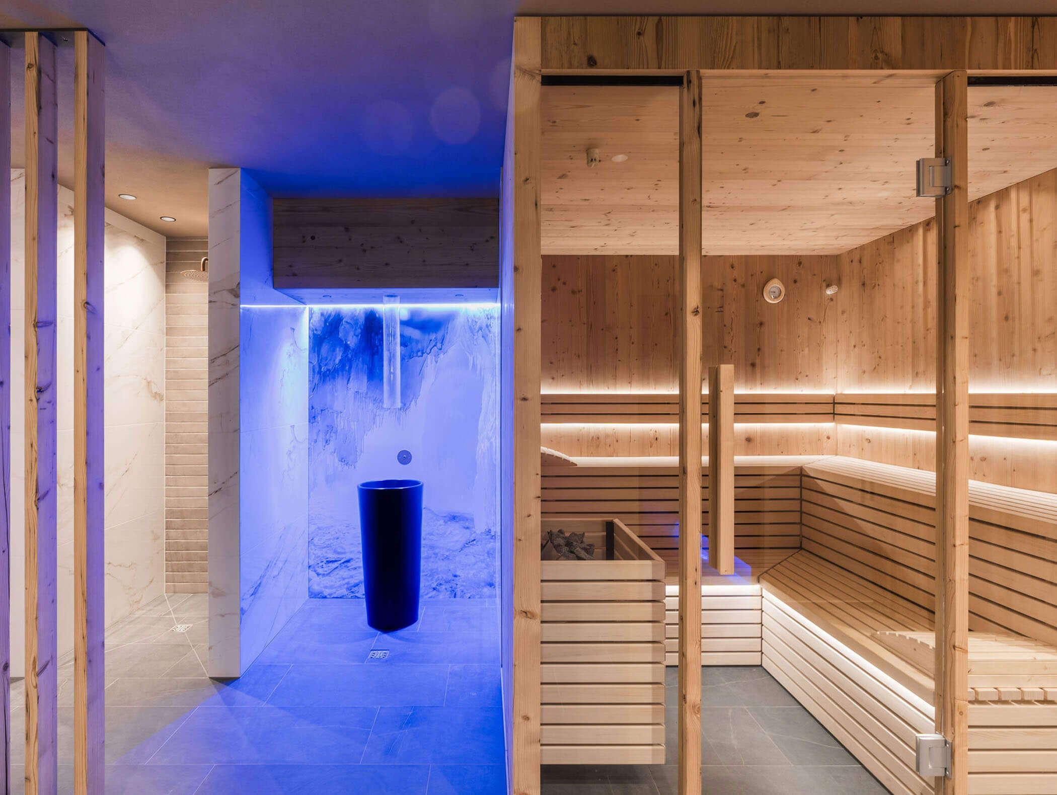 Moderne Saunakabine mit Holzbänken und -wänden, daneben ein Spa-Bereich mit blauer LED-Beleuchtung. - Majestic Resorts (Relaunch)