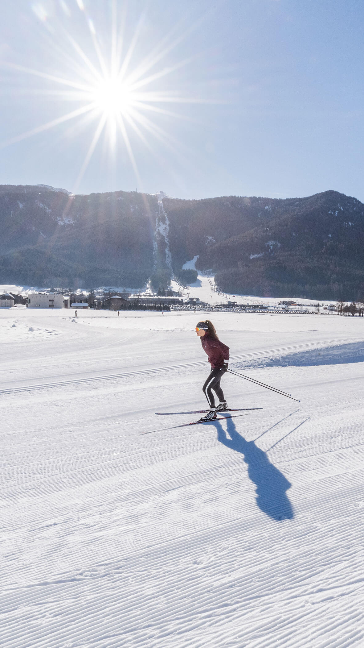 Eine Person beim Skilanglauf auf einem verschneiten Feld unter strahlender Sonne mit Bergen im Hintergrund. - Majestic Resorts (Relaunch)