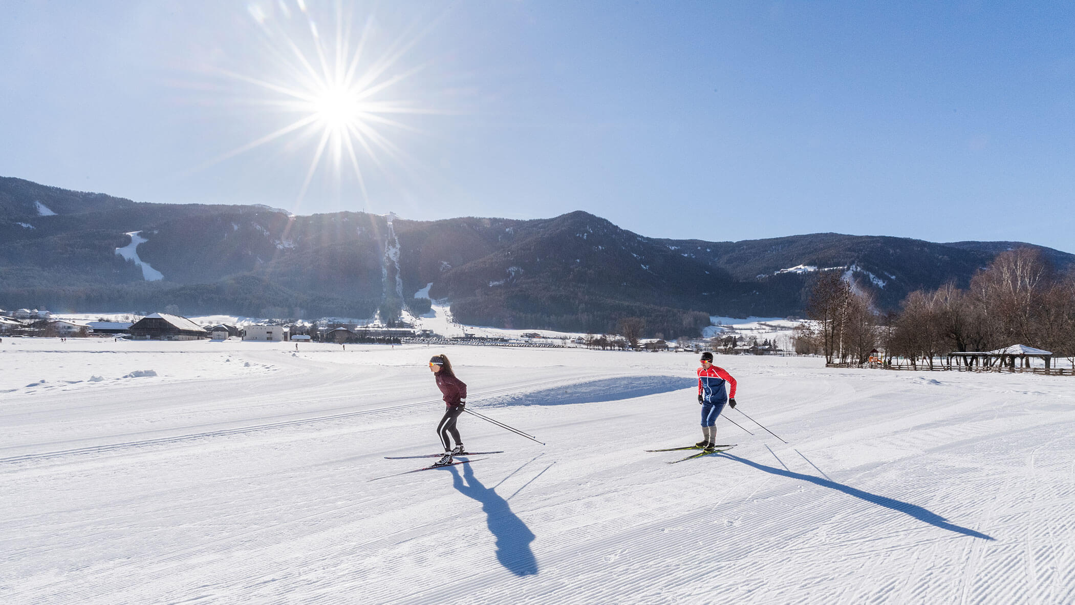 Zwei Personen beim Skilanglauf in einer sonnigen, verschneiten Landschaft mit Bergen im Hintergrund. - Majestic Resorts (Relaunch)