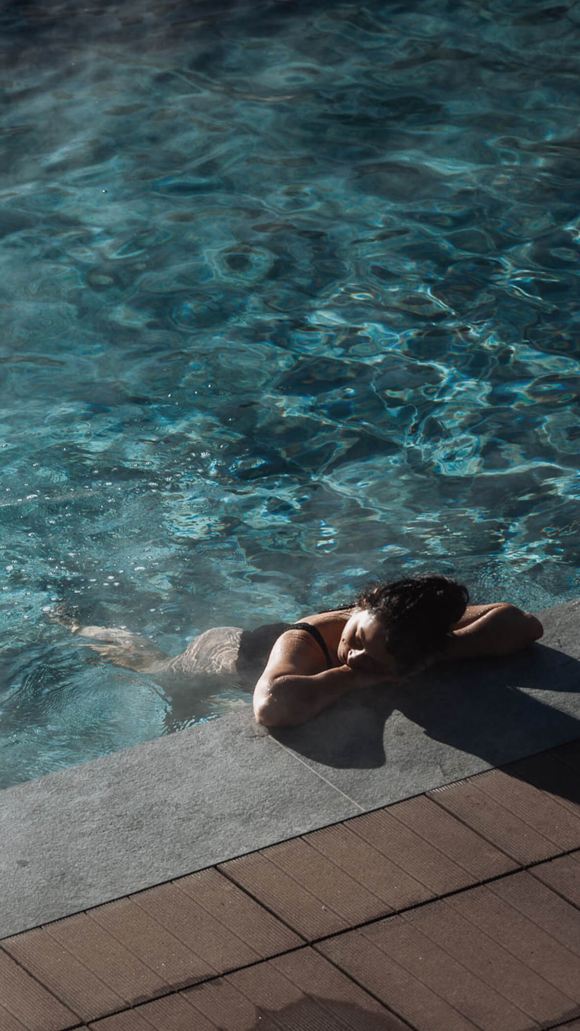 Person, die sich am Rande eines Swimmingpools entspannt, die Arme auf dem Beckenrand verschränkt, mit Sonnenlicht auf dem Wasser. - Majestic Resorts (Relaunch)