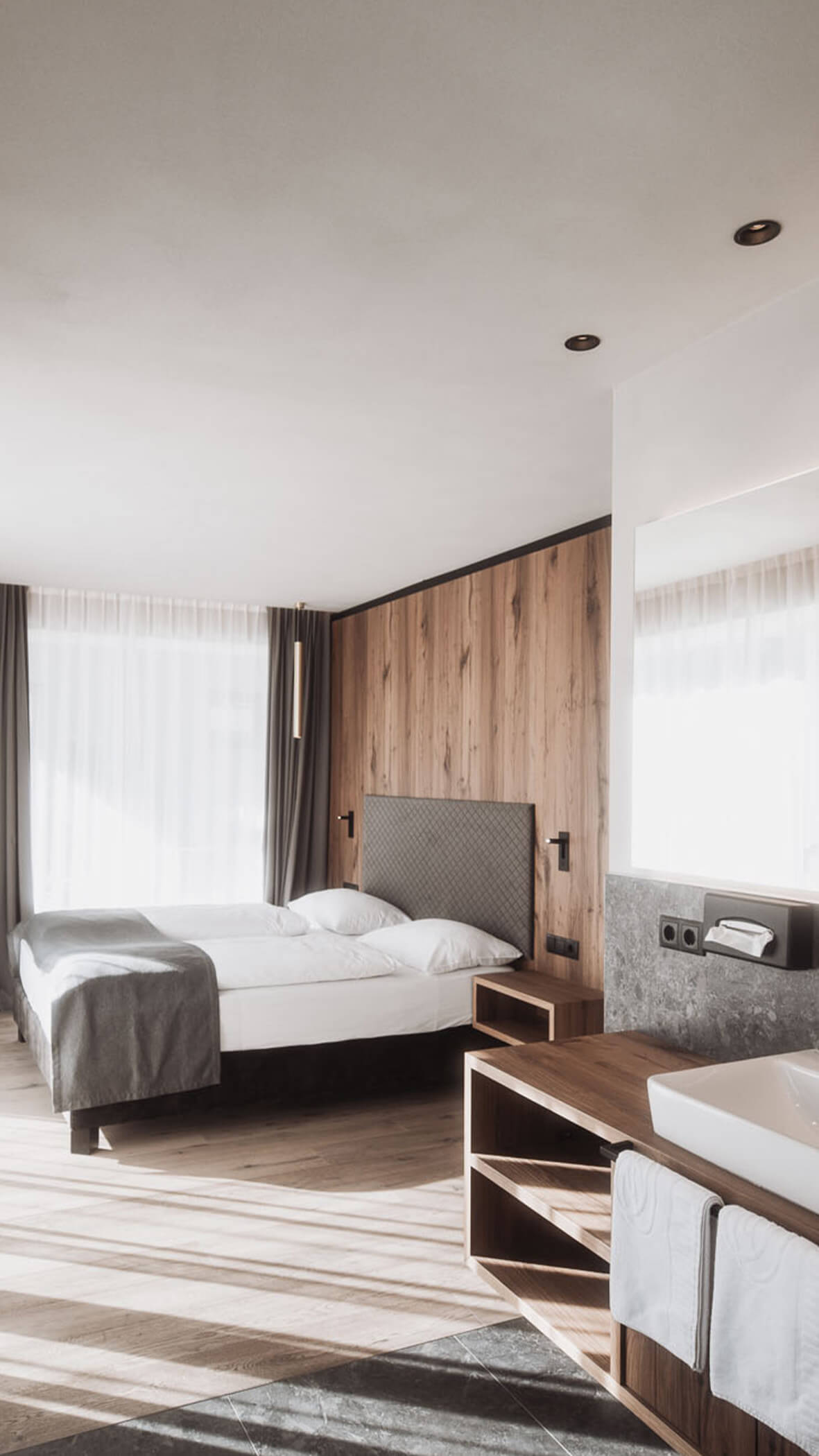 Minimalistisches Hotelzimmer mit einem großen Bett, Holzakzenten, einem großen Fenster und einem Waschbecken im Vordergrund. - Majestic Resorts (Relaunch)