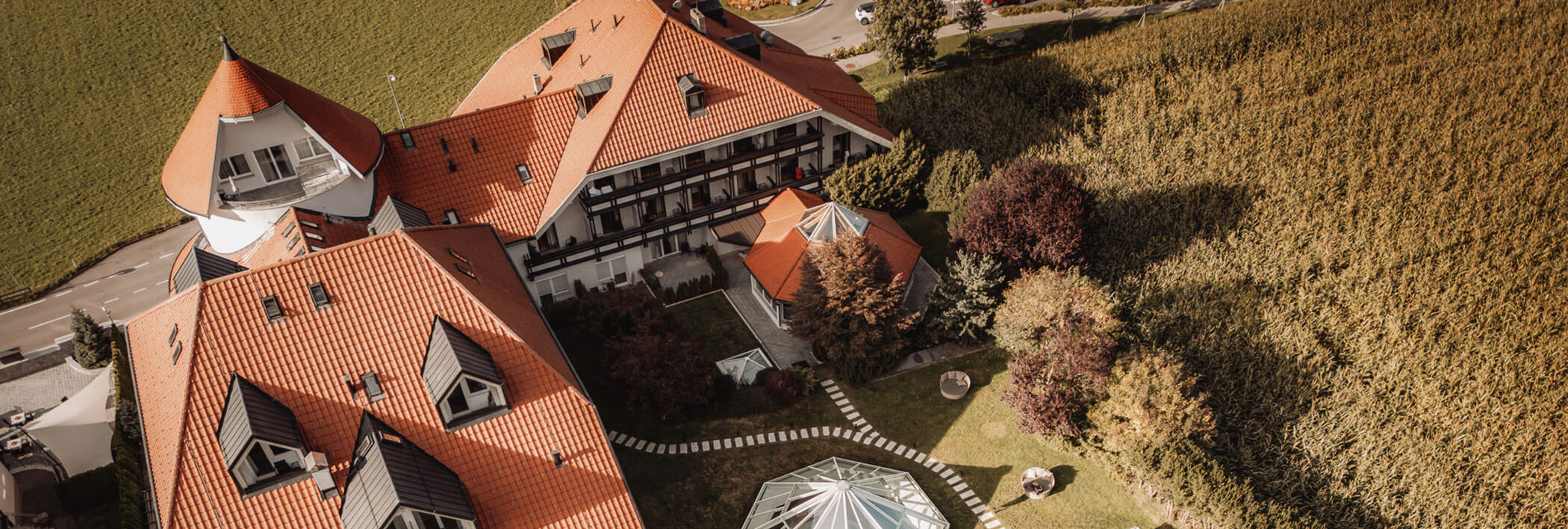 Luftaufnahme eines großen Gebäudes mit roten Dächern neben Feldern und einem angelegten Garten. - Majestic Resorts (Relaunch)